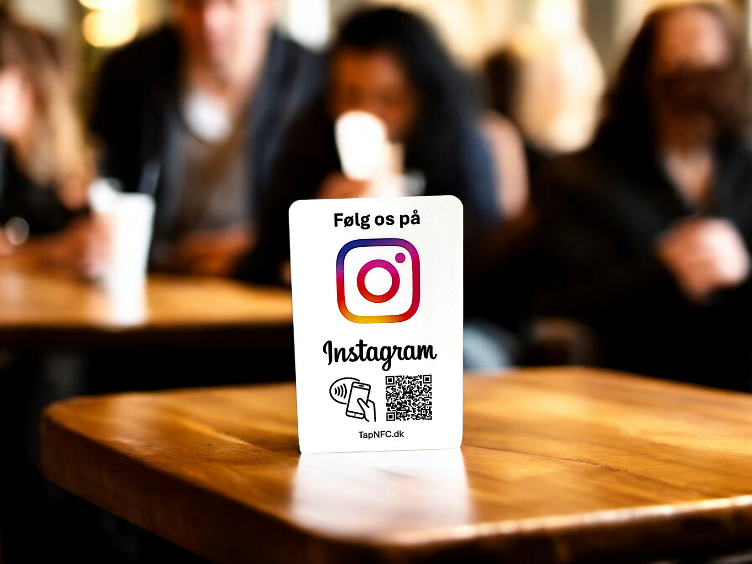 En bordstander med teksten "Følg os på Instagram". Bordstanderen indeholder også NFC og QR-kode. Kan ses på et træbord i en butik